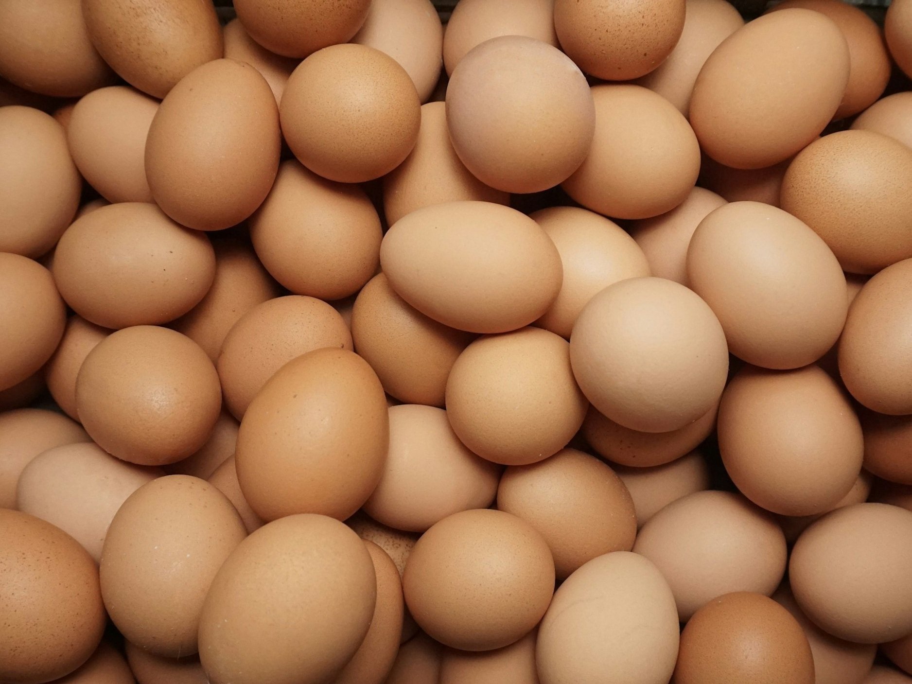 A close-up view of a large pile of brown eggs, showcasing their smooth surfaces and varied shades, ideal for culinary uses and baking.