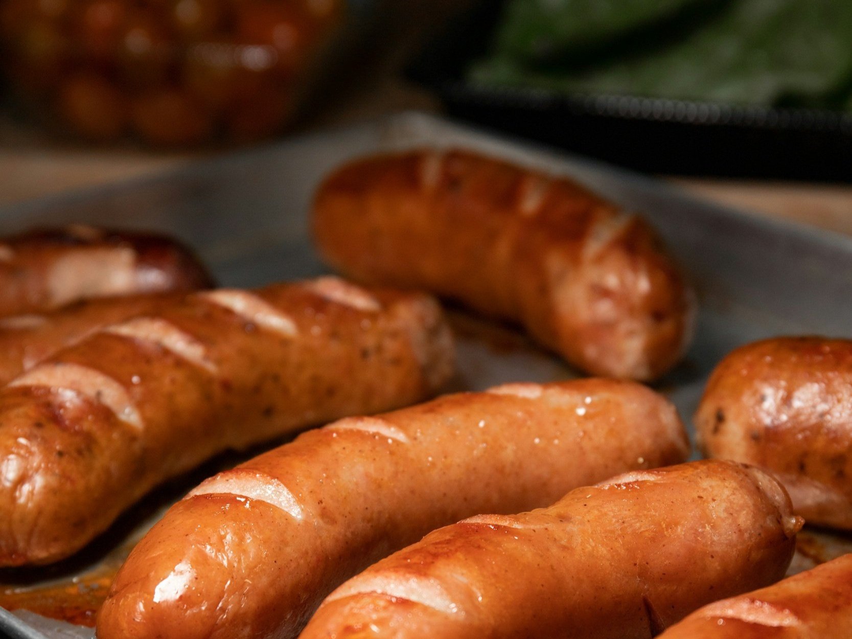 Grilled sausages on a metal tray, showcasing various types with a glossy finish, perfect for barbecues or hearty meals.